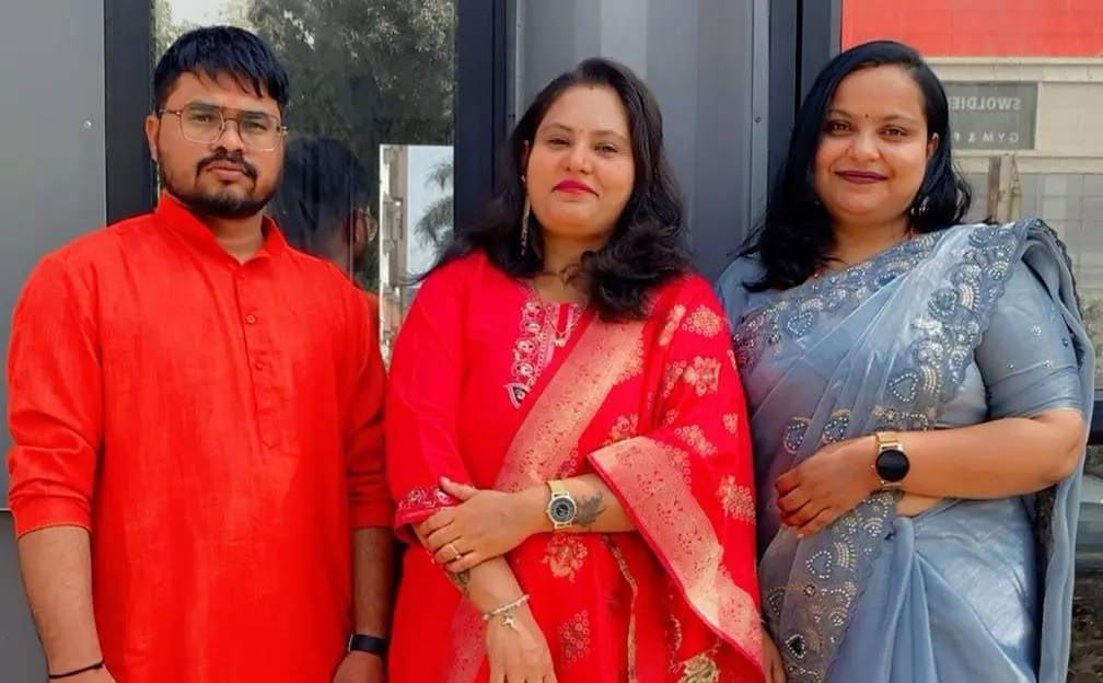 Woman in vibrant pink saree with two men in orange and green kurtas.