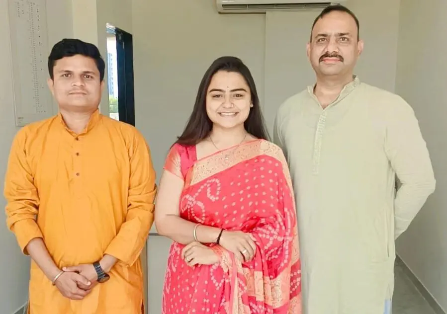 Woman in pink Bandhani saree standing between two male colleagues in kurtas.